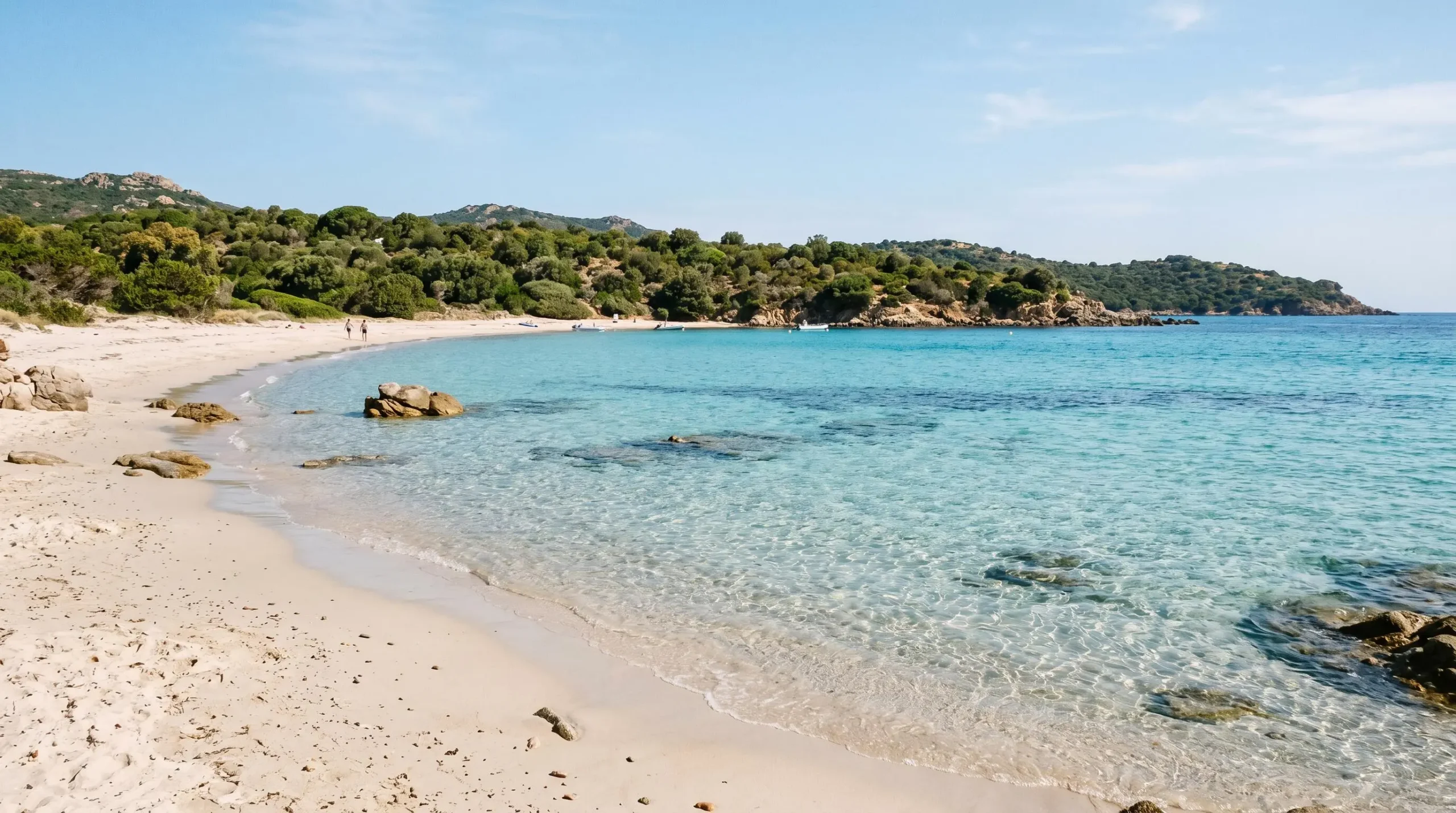 Plage de Bodri à l'Île-Rousse avec sable clair, eaux turquoise transparentes, rochers côtiers et végétation méditerranéenne en arrière-plan sous lumière naturelle